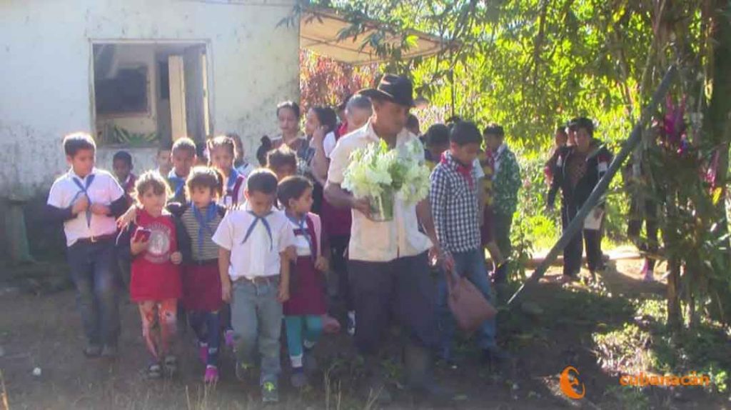 Genaro y los niños colocan las flores en homenaje al Maestro.